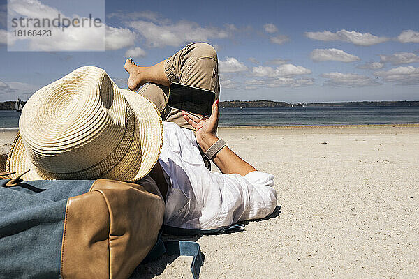 Reife Frau nutzt ihr Smartphone und entspannt sich an einem sonnigen Tag am Strand