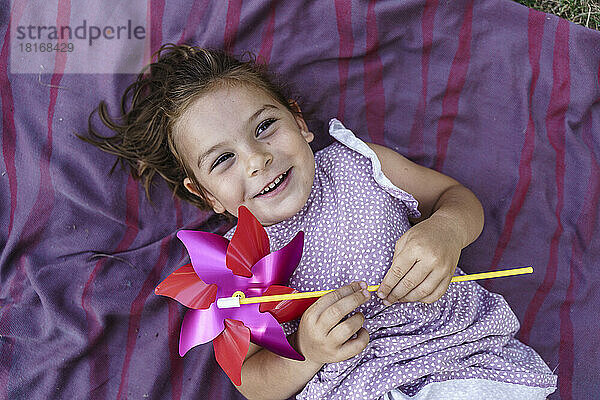 Happy girl holding pinwheel toy lying on blanket