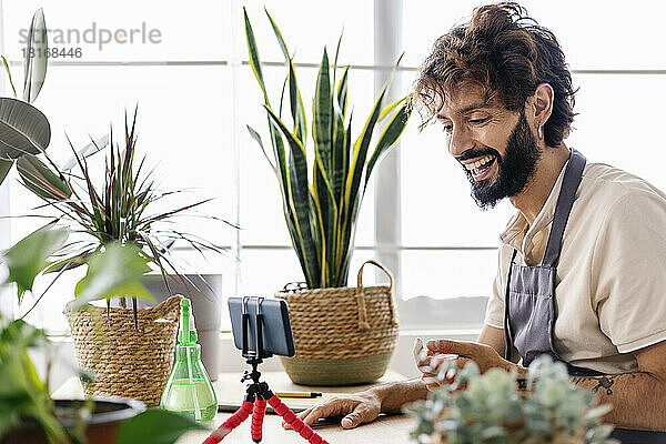 Glücklicher Mann mit Smartphone auf Stativ im Pflanzenladen