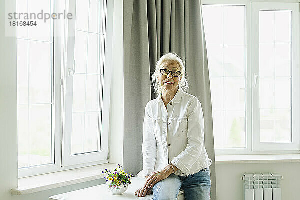 Ältere Frau sitzt zu Hause am Tisch am Fenster