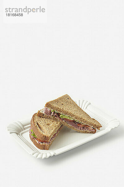 Scheiben Schwarzbrot-Schinken-Sandwich auf Tablett vor weißem Hintergrund