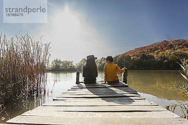 Boy and girl sitting on jetty on sunny day