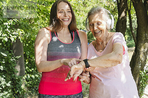 Fröhlicher Fitnesstrainer mit Seniorin mit Smartwatch im Park