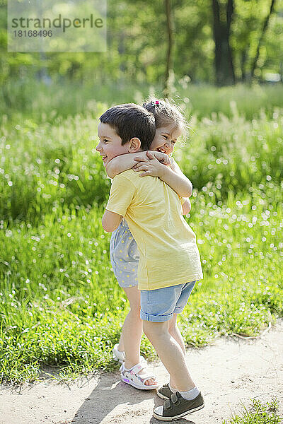 Glückliches Mädchen umarmt Bruder im Park an einem sonnigen Tag