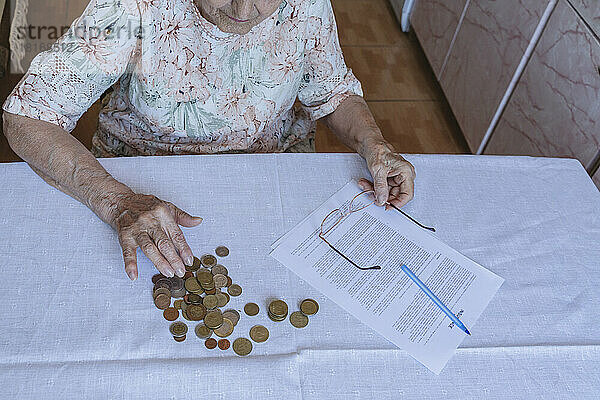 Senior woman counting coins by home finance documents on table