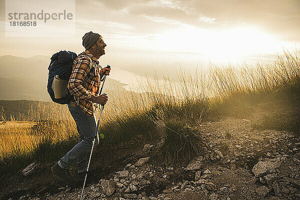 Glücklicher reifer Mann mit Rucksack beim Wandern bei Sonnenaufgang