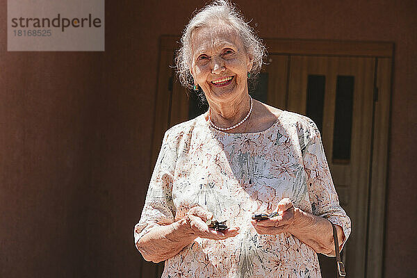 Lächelnde ältere Frau mit Autoschlüsseln vor dem Haus