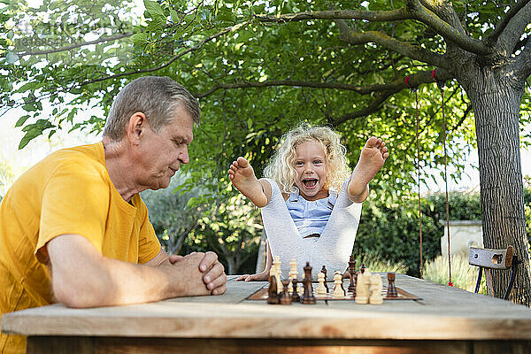 Glückliches Mädchen  das es genießt  wenn sein Großvater auf dem Tisch im Garten Schach spielt