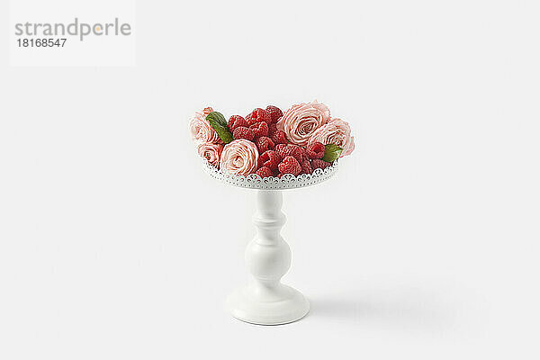Raspberries with pink roses on pedestal cakestand against white background
