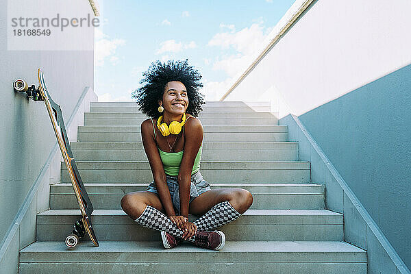 Glückliche junge Frau sitzt mit Skateboard auf Stufen