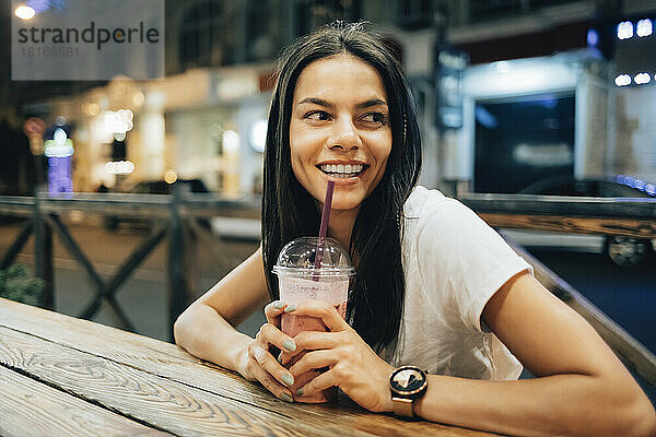 Glückliche schöne Frau mit Smoothie-Drink sitzt im Straßencafé