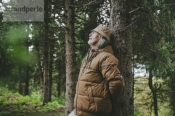 Nachdenklicher Mann steht am Baum im Wald