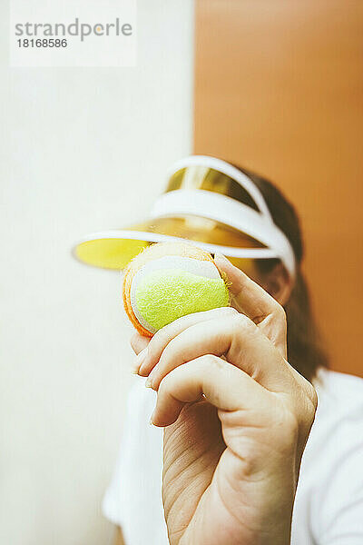 Frau hält Tennisball vor zweifarbigem Hintergrund