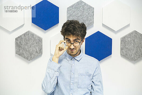 Businessman wearing eyeglasses in front of designed wall at work place