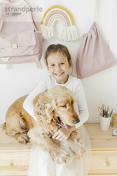 Happy girl embracing dog sitting on cabinet