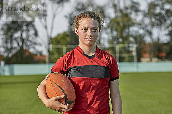 Selbstbewusstes Mädchen mit Rugbyball steht auf dem Feld
