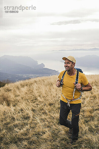 Lächelnder reifer Mann mit Mütze beim Wandern auf dem Berg