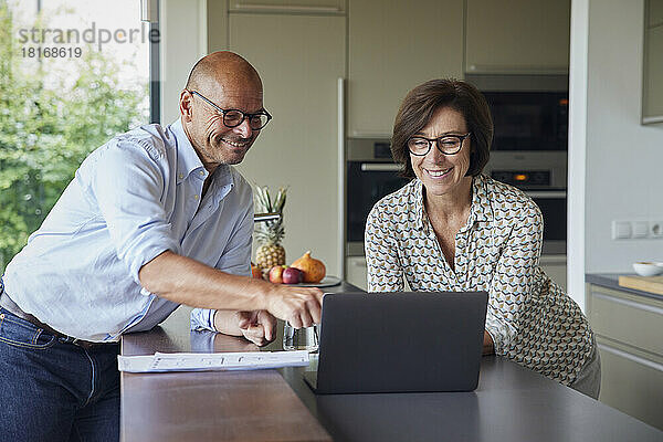 Glücklicher Mann und Frau  die zu Hause einen Laptop auf der Küchentheke benutzen