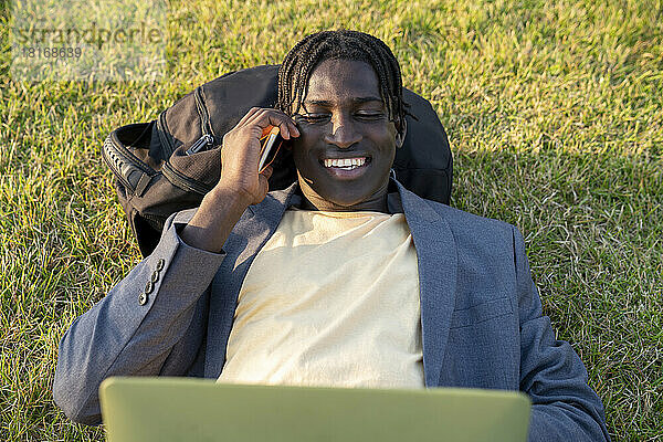 Lächelnder Geschäftsmann  der am Handy liegt und mit Laptop spricht