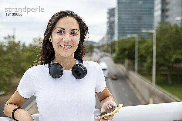 Lächelnde schöne Frau mit Mobiltelefon am Geländer gelehnt