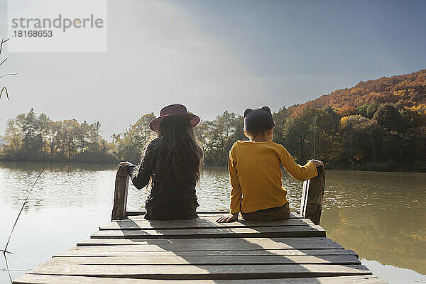 Boy and girl sitting on jetty at lake