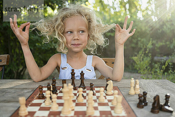 Cute girl playing with hair sitting in front of chessboard