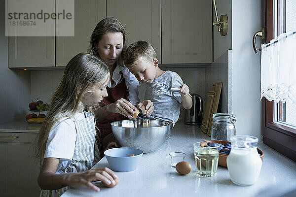 Mutter und Kinder bereiten zu Hause in der Küche Kuchen zu