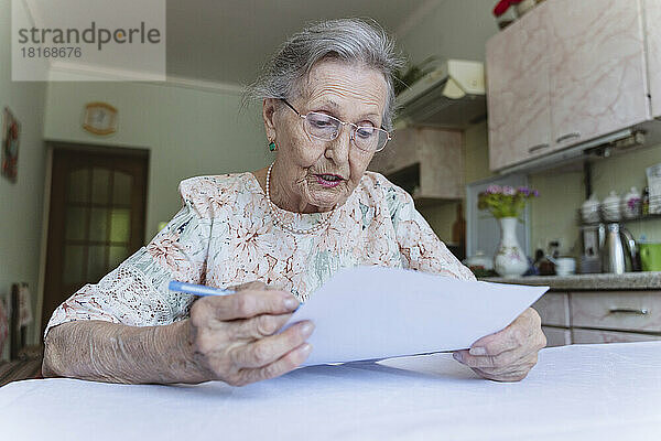 Ältere Frau liest am Tisch zu Hause den Vertrag