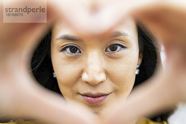 Smiling woman looking through hands making heart shape