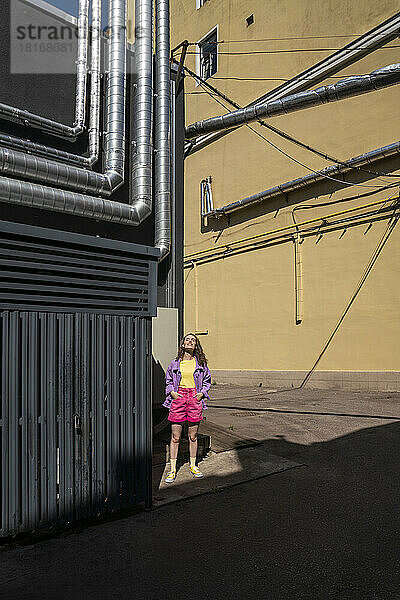 Frau steht an sonnigem Tag in der Nähe eines Gebäudes mit Rohren