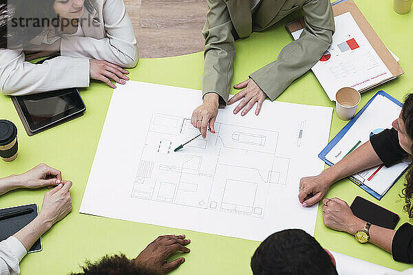 Businesswoman explaining floor plan to colleagues on table