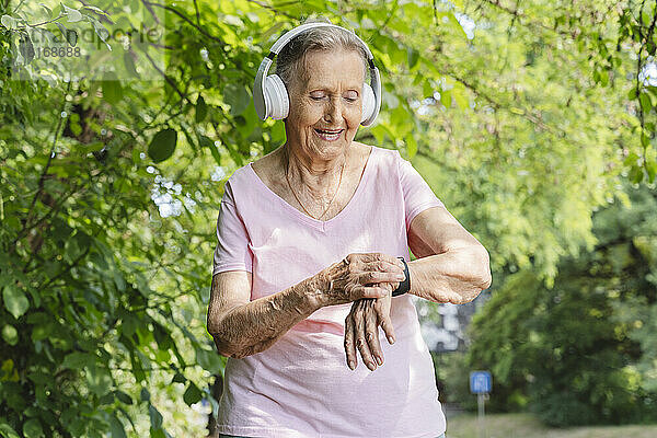 Lächelnde ältere Frau mit Smartwatch  die im Park Musik über Kopfhörer hört