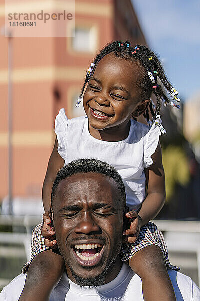 Schreiender Mann  der an einem sonnigen Tag seine Tochter auf den Schultern trägt
