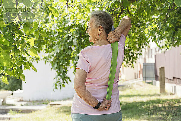 Ältere Frau trainiert mit Widerstandsband inmitten von Bäumen