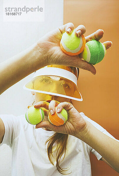 Tennis player holding sports balls against colored background