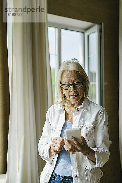 Ältere Frau schreibt zu Hause Textnachrichten über ihr Smartphone