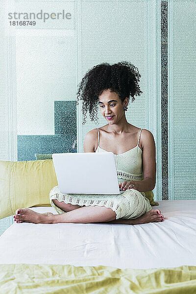 Frau mit lockigem Haar benutzt Laptop zu Hause im Bett