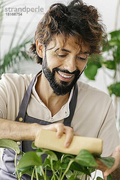 Lächelnder Mann reinigt Pflanzenblätter mit Serviette im Geschäft