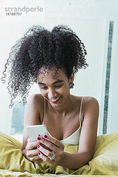 Happy curly-haired woman using smart phone at home