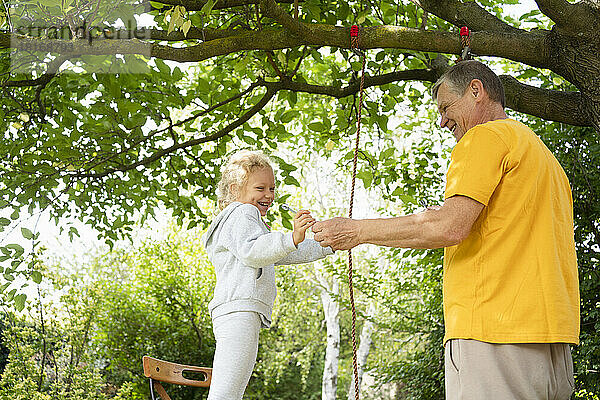 Großvater und Enkelin schaukeln mit Seil im Garten
