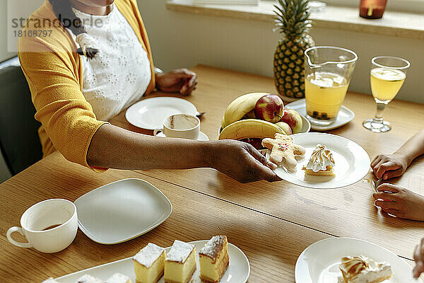Hand of woman holding plate of lemon meringue pie and gingerbread at dining table