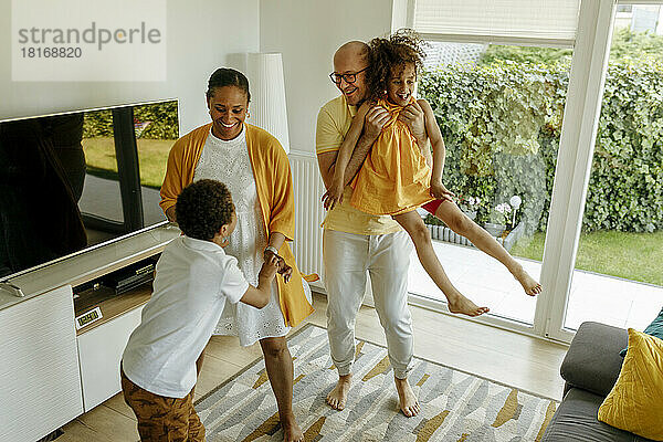 Happy parents with children dancing in living room at home