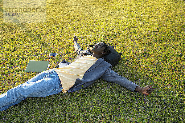 Lächelnder Geschäftsmann mit Mobiltelefon und Laptop entspannt im Gras