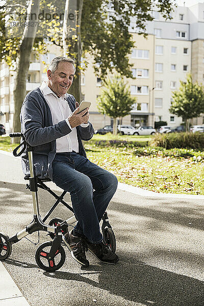 Smiling senior man using smart phone sitting on mobility walker