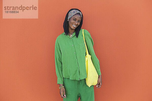 Glückliche Frau mit Einkaufstasche steht vor orangefarbener Wand