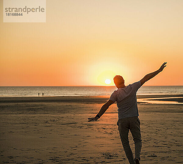 Mann mit ausgestreckten Armen amüsiert sich am Strand bei Sonnenuntergang