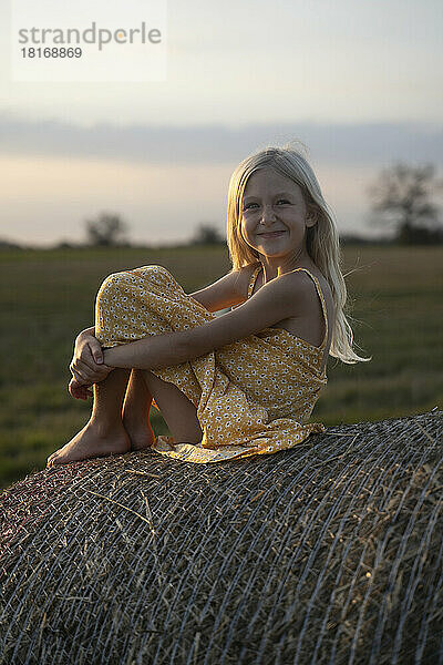 Smiling cute girl with blond hair sitting on haystack