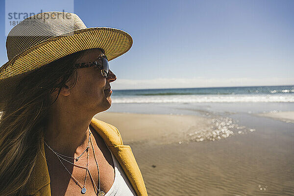 Reife Frau mit Hut und Sonnenbrille am Strand an einem sonnigen Tag