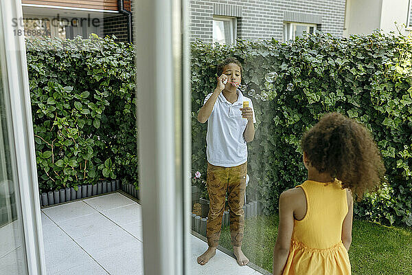 Mädchen blickt auf Bruder  der auf der Terrasse Seifenblasen bläst