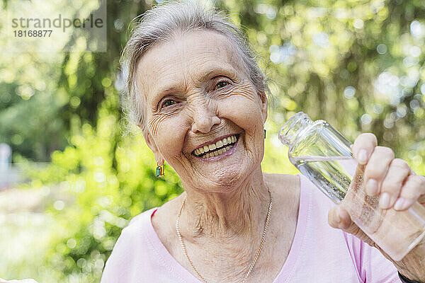 Fröhliche ältere Frau hält Wasserflasche im Park